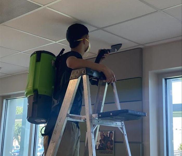 SERVPRO Team member on a ladder cleaning ceiling tiles in a commercial building